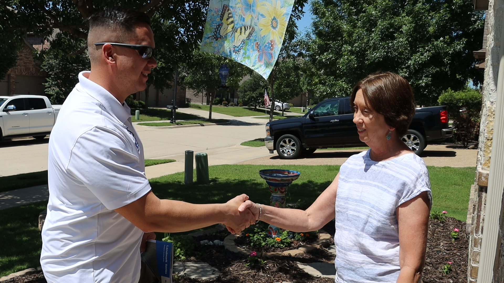 A roofing professional shaking hands with a homeowner outside her home